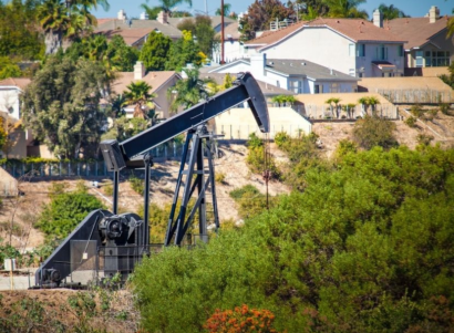 Oil and gas well in hills surrounded by trees and homes.