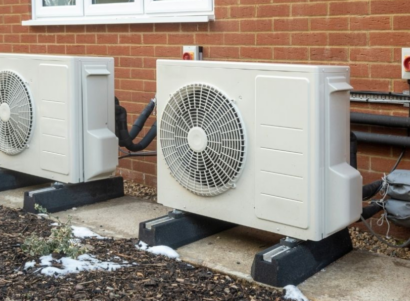 Two heat pumps outside in front of brick wall